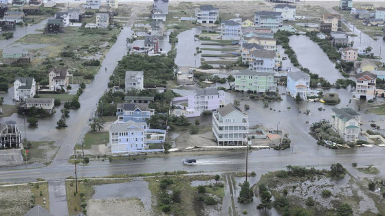 Aerial view of a flooded coastal neighborhood with beach houses surrounded by stormwater after a hurricane.